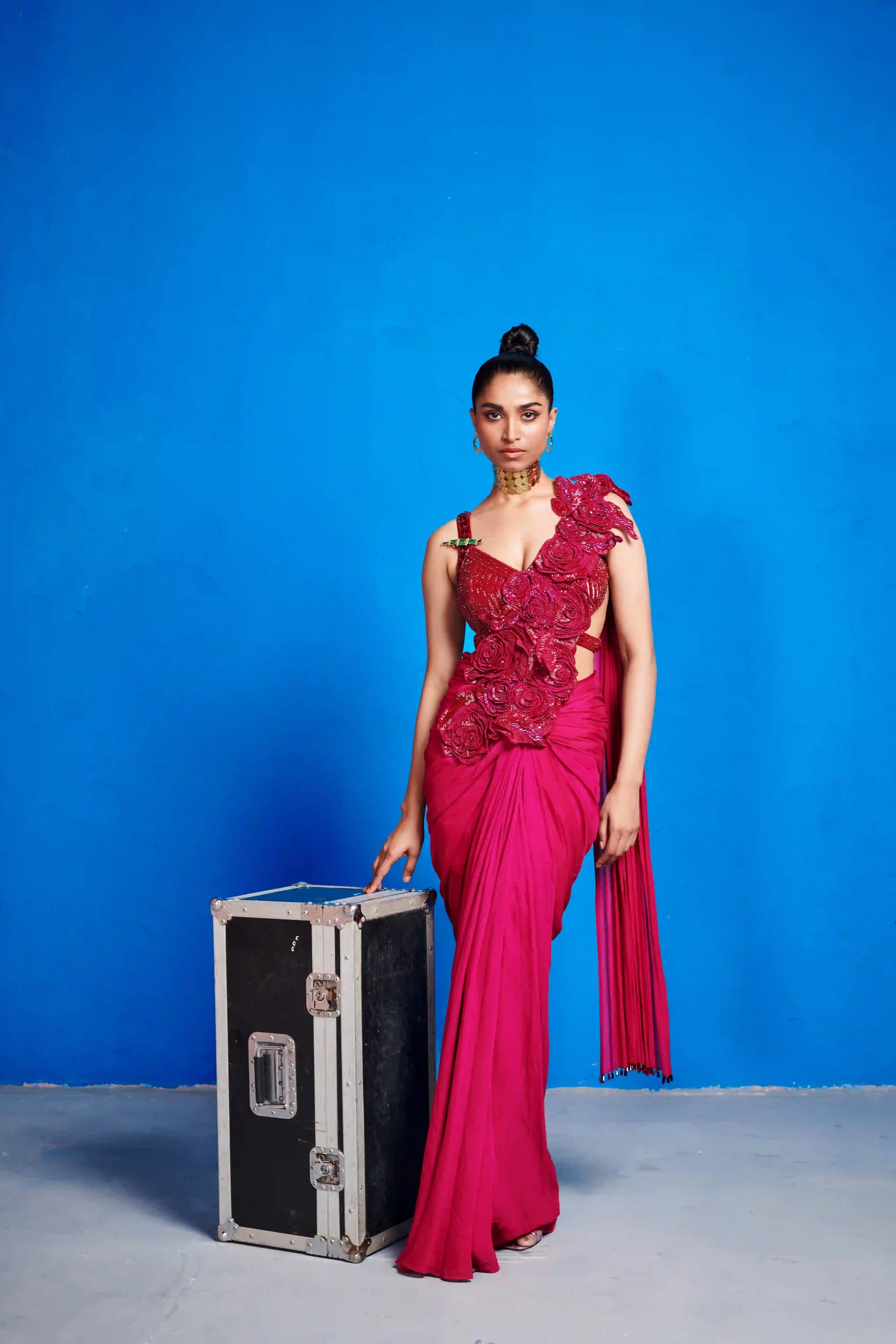 Woman in a pink saree with floral details holding against a blue background